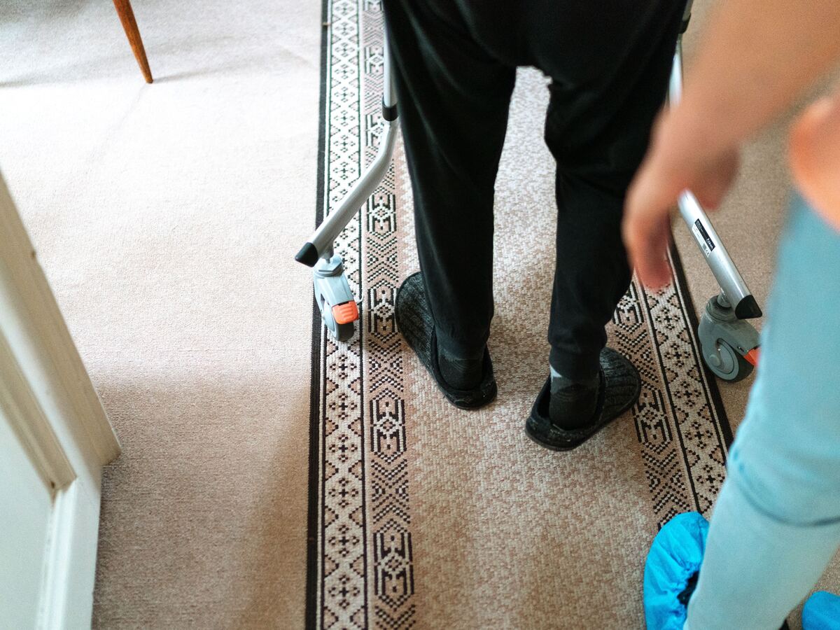Close-up of a client using a walking frame with a carer close by for support