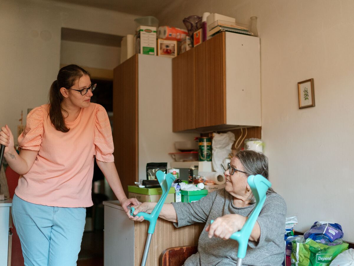 Carer supporting a client with mobility aids in the home, chatting as they help